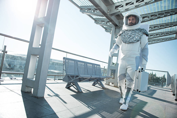 Smiling spaceman carrying small suitcase - 写真・画像