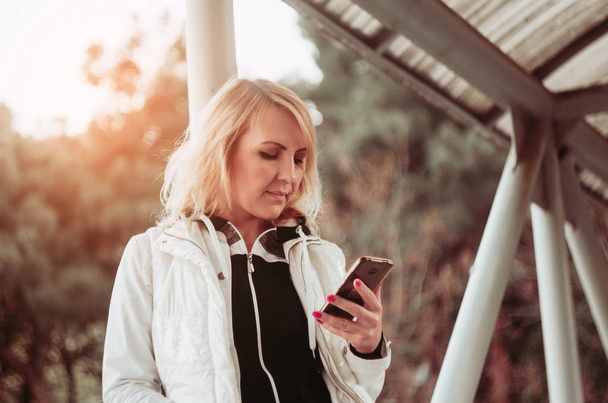 Blonde Frau auf der Brücke mit Smartphone. Herbstzeit - Foto, Bild