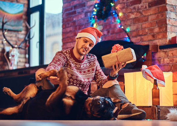 Ελκυστική γενειοφόρος hipster αρσενικό με τον σκύλο του Rottweiler σε ένα δωμάτιο με Χριστουγεννιάτικη διακόσμηση. - Φωτογραφία, εικόνα
