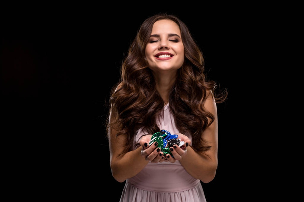 Sexy krullend haar brunette poseren met chips in haar handen, poker concept zwarte achtergrond - Foto, afbeelding