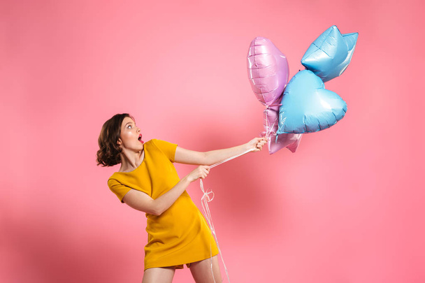 Confused young woman in yellow dress holding ballons - 写真・画像