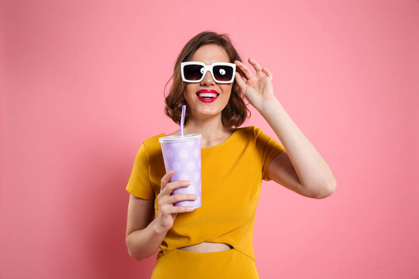 Portrait of a cheerful girl in sunglasses holding cup - 写真・画像