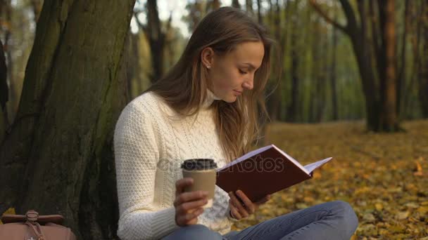 Female student reading book, sitting in beautiful park on warm autumn day - Video