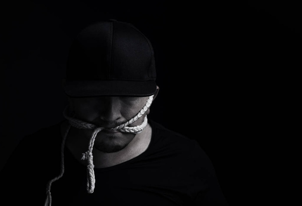 man with cap bite a rope in front of black background - Foto, afbeelding