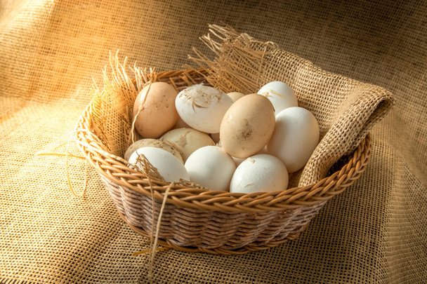 Fresh organic Hen eggs in basket wrapped with burlap fabric material and with direct morning sunshine light effect. - Photo, Image