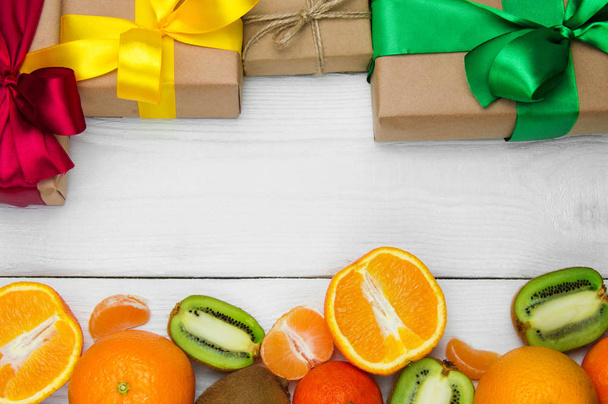 Frutta arancio, mandarino e kiwi e confezione regalo con fiocco a nastro su sfondo bianco retrò in legno
 - Foto, immagini