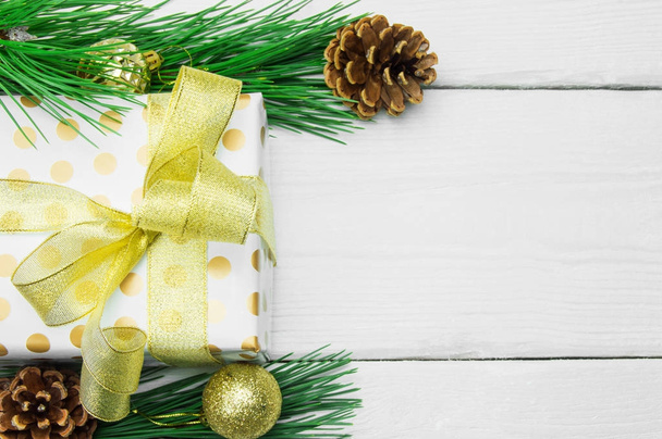 Caja de regalo con lazo de cinta de oro y rama árbol de Navidad con cono sobre fondo vintage de madera blanca
 - Foto, Imagen