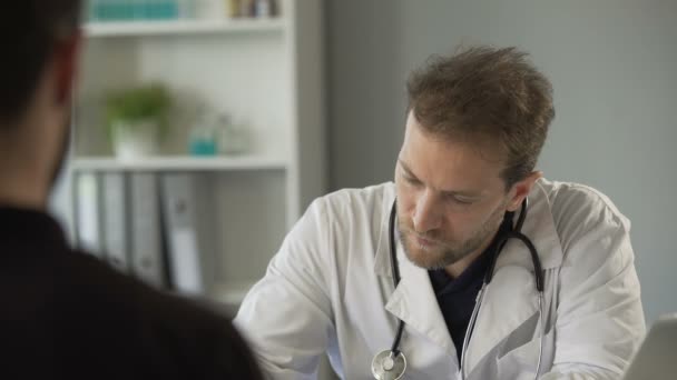 Male physician talking with patient and listening to heartbeat with stethoscope - Filmagem, Vídeo