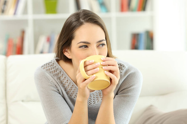 Woman drinking coffee looking at side at home - Foto, afbeelding