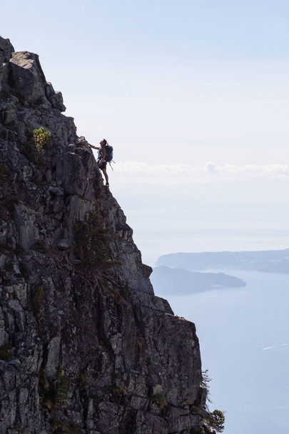 Adventurous male hiker is climbing a steep rocky hill on top of the mountain. Picture taken at Lions Peak hike in Lions Bay, North of Vancouver, British Columbia, Canada. - 写真・画像