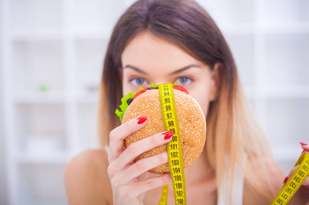 A young woman holding a burger in a measuring tape. A girl stand - 写真・画像