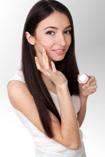 Bella giovane donna che applica la crema viso al suo osso della guancia in un
 - Foto, immagini