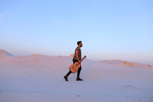 Величні мусульманських молода людина прогулянки з гітара в руках через dese - Фото, зображення