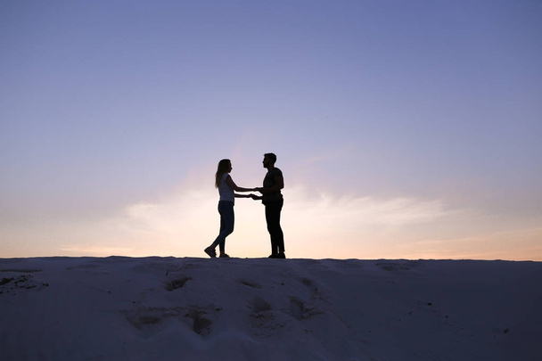 Любовники держат друг друга за руки и кружатся на песчаном холме в пустыне на
 - Фото, изображение
