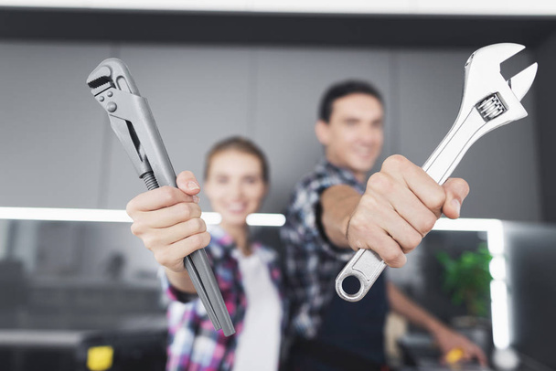 A man and a woman plumber will be cheated in the kitchen. They show the wrenches in the camera. - Fotoğraf, Görsel