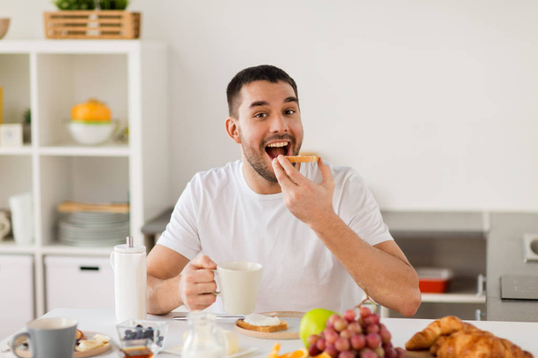 άνθρωπος τρώει τοστ με καφέ στην κουζίνα στο σπίτι - Φωτογραφία, εικόνα