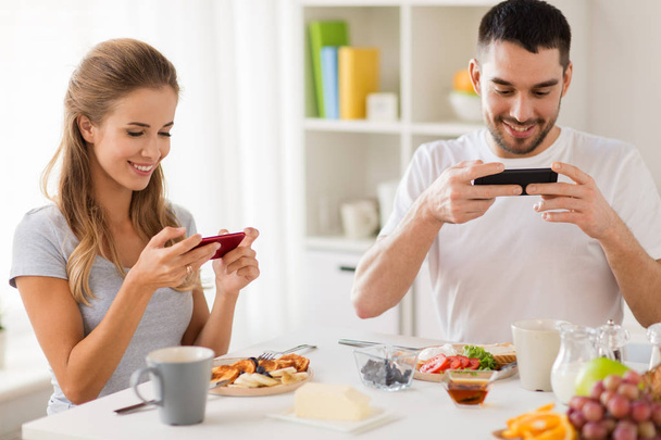 couple with smartphones having breakfast at home - Foto, Imagem