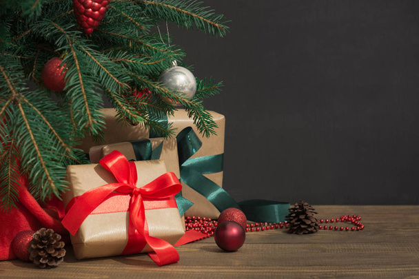 Weihnachtsurlaub Hintergrund. Geschenke mit roter Schleife, Weihnachtsmütze und Dekor unter einem Weihnachtsbaum auf einem Holzbrett. - Foto, Bild