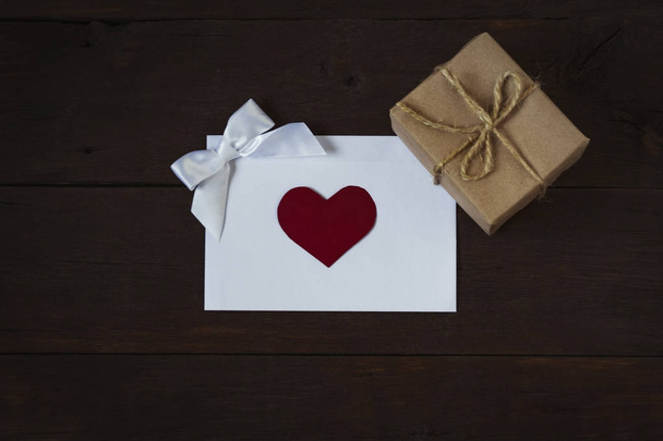Umschlag mit einem Herz, einer verschwenderischen Schleife und einer Geschenkbox auf einem taufrischen Bac - Foto, Bild