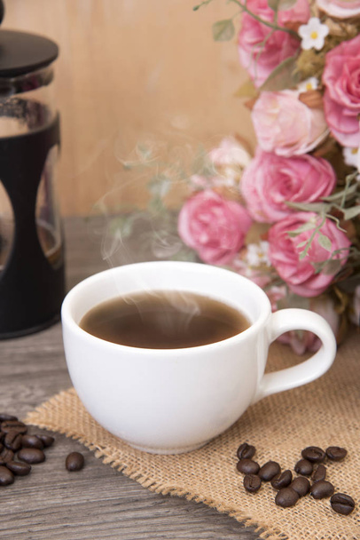 heiße Tasse Kaffee auf Holztisch mit Rosenblüte. Konzept Kaffee - Foto, Bild