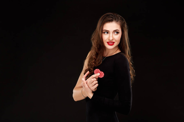 Σέξι σγουρά μαλλιά μελαχρινή ποζάρουν με τσιπ στα χέρια της, πόκερ έννοια μαύρο φόντο - Φωτογραφία, εικόνα