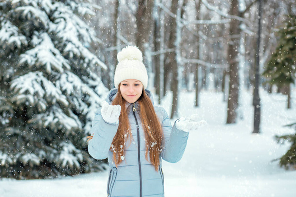 A girl dressed in warm winter clothes and a hat posing in a winter forest. Model with a beautiful smile near the Christmas tree. - Fotó, kép