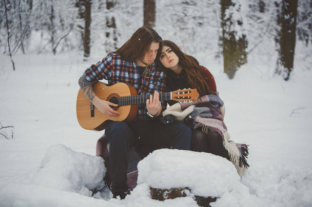 Man plays guitar to his girlfriend in winter forest - Foto, Imagen