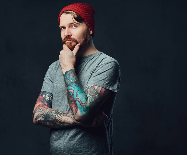 Redhead vousatý muž s tetováním na ruce představují šedé pozadí. - Fotografie, Obrázek