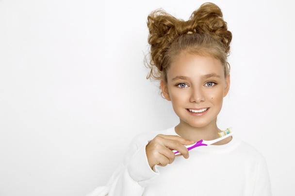 Cute, beautiful blonde, young girl holding a toothbrush and smiling happily. The girl is washing her teeth. - Photo, Image