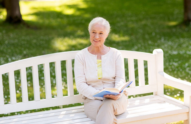 happy senior woman reading book at summer park - Valokuva, kuva