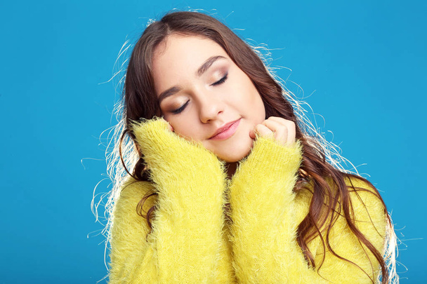 Beautiful young girl in yellow sweater on blue background - Foto, imagen