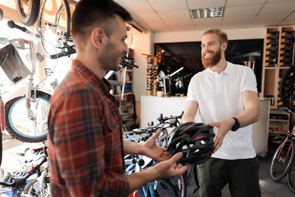 The man-seller shows the buyer a helmet for bike rides. - Fotó, kép