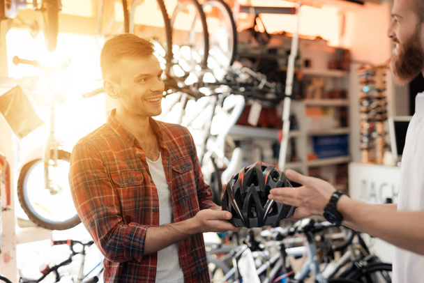 The man-seller shows the buyer a helmet for bike rides. A young man came to the bicycle store. The consultant talks about this product. - Foto, Bild