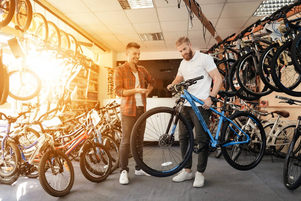 Bir satıcı bir bisiklet mağazada yeni bir dağ bisikleti seçin bir genç alıcı yardımcı olur.. - Fotoğraf, Görsel