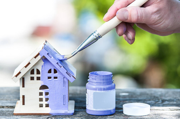 Hand with brush paints a toy house in lavender color, the backgr - Photo, Image