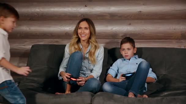 Anne ve iki oğlu kablosuz joystick ile video oyunları oynarken onun evinde kanepede oturuyor. Evde mutlu insanlar. - Video, Çekim