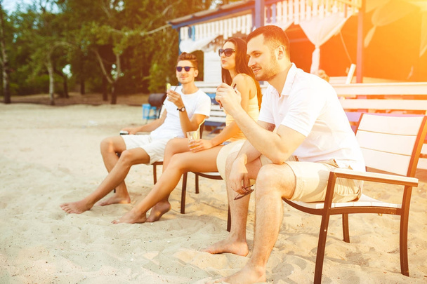Молоді люди насолоджуються літнім відпочинком сонячними ваннами, які п'ють у пляжному барі
 - Фото, зображення