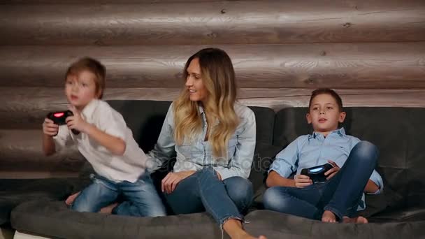Anne ve iki oğlu kablosuz joystick ile video oyunları oynarken onun evinde kanepede oturuyor. Evde mutlu insanlar. - Video, Çekim
