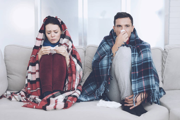 The couple is sitting on the couch wrapped in blankets. Man and woman are sick. The man flies out. Woman holding napkin - Photo, Image