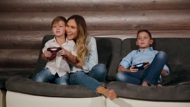 Mère et deux fils assis sur le canapé dans sa maison jouant à des jeux vidéo avec joystick sans fil. Des gens heureux dans la maison
. - Séquence, vidéo