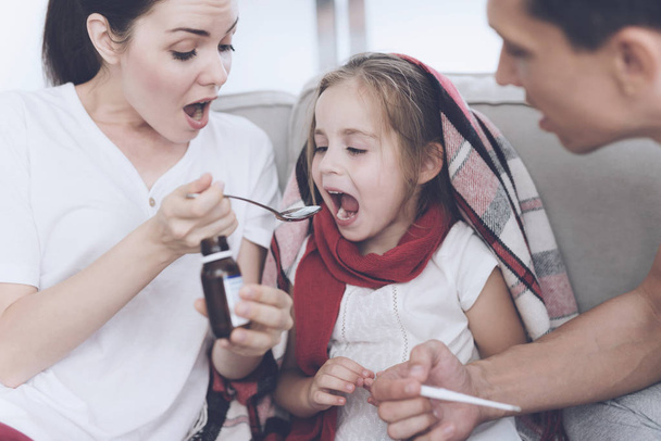 The little girl caught a cold. Her mother and father are treating her. Mother pours a girl syrup into a spoon - Foto, afbeelding