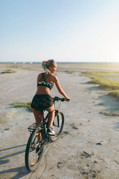カラフルなスーツでスポーティな金髪女性、サボテンで自転車に乗る - 写真・画像