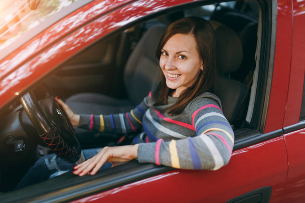 Piękne młode, które szczęśliwy uśmiechający się kobiety Brunet z czystą i zdrową skórę ubrany w t-shirt w paski siedzi w samochodzie czerwony z czarnym wnętrzem. Podróży i jazdy koncepcja. - Zdjęcie, obraz