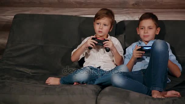Dois irmãos sentados no sofá e muito emotivos jogando videogames com joystick sem fio
. - Filmagem, Vídeo