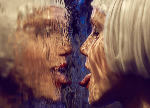 Close up futuristic neon lighted portrait of a girl with white bob hairstyle licking wet glass  - Фото, зображення