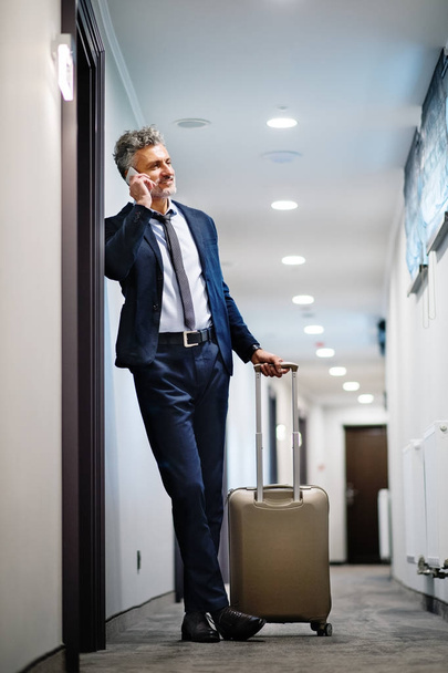 Hombre de negocios maduro con smartphone en un pasillo de hotel
. - Foto, Imagen