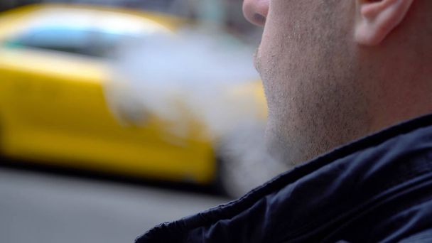 Jonge duizendjarige stedelijke hipster waait damp elektronische sigarettenrook buiten op New York City Street in Day time. Gele taxi cab gaat in de achtergrond. Over de schouder POV Bekijk - Foto, afbeelding