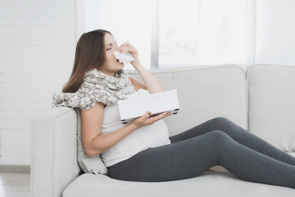Sick pregnant woman sitting at home on the couch. She flies herself into a paper napkin. - Photo, Image