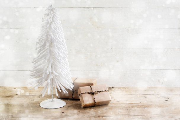 vánoční stromeček z bílý drát a dary v kraft papír na rustikální dřevěný stůl, bílé malované vintage pozadí zasněžené bokeh světel, kopie prostor - Fotografie, Obrázek