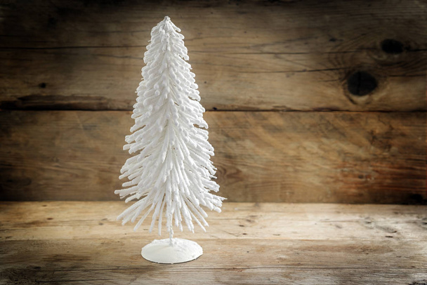 kleiner Weihnachtsbaum aus weißem Flockendraht vor rustikalem Holzhintergrund mit großem Kopierraum - Foto, Bild